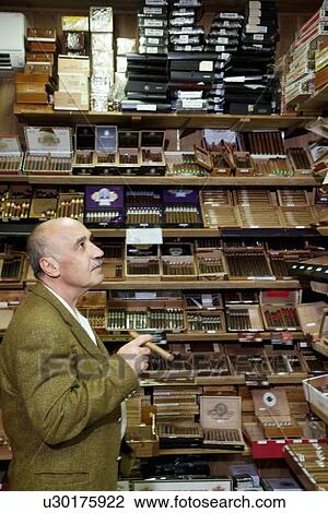 Stock Image - Mature tobacco shop owner looking at cigars on display. Fotosearch