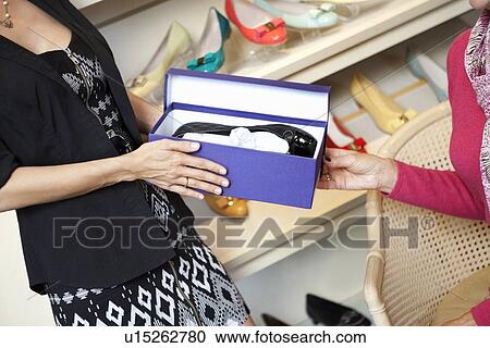 Mid adult woman giving footwear to mature customer in shoe store View Large Photo Image Stock Image - Mid adult woman giving footwear to mature customer in shoe store. Fotosearch