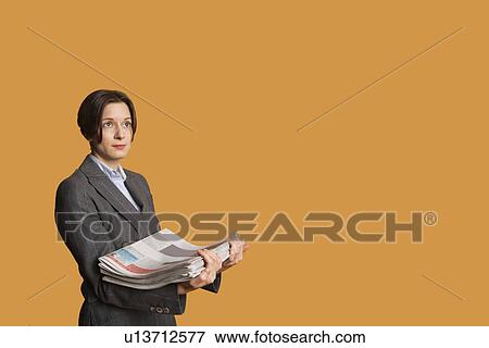 Stock Photo - Mid adult woman holding stack of newspapers. Fotosearch