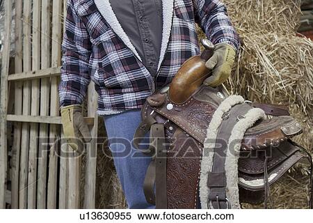 Stock Photography - Midsection of a mature man holding horse riding tack. Fotosearch