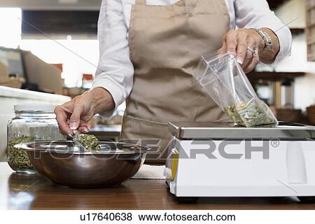 Stock Photo - Midsection of an employee measuring ingredient on weight scale in spice store. Fotosearch