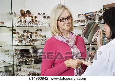 Stock Image - Optician holding mirror while senior female customer looking. Fotosearch
