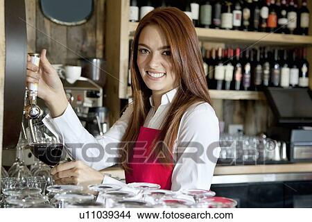 Picture - Portrait of a beautiful young waitress removing wine in bar. Fotosearch
