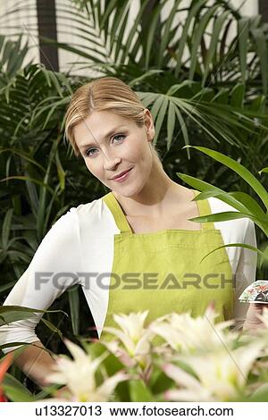 Stock Image - Portrait of a beautiful young woman in greenhouse. Fotosearch