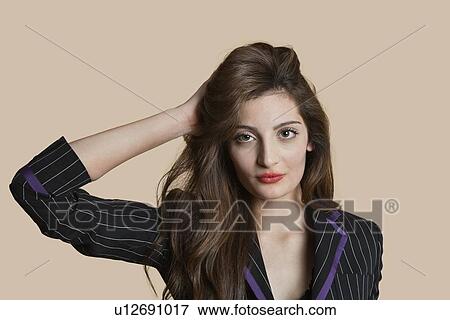 Stock Photo - Portrait of a beautiful young woman with hand in hair over colored background. Fotosearch
