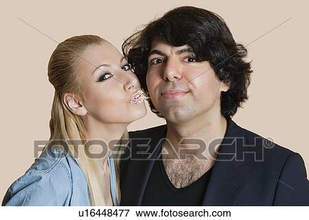 Stock Photo - Portrait of a blond woman with sprinkled lips kissing young man over colored background. Fotosearch