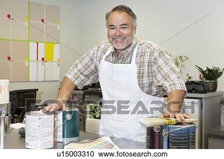 Stock Image - Portrait of a cheerful mature sales clerk with paint can in hardware store. Fotosearch