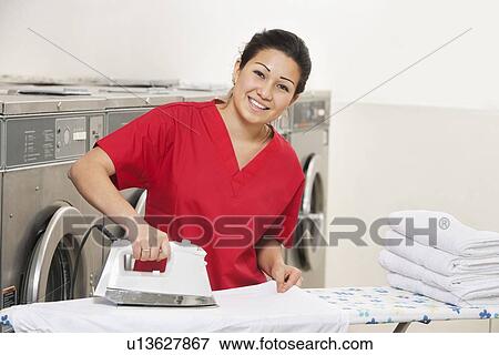 Stock Photo - Portrait of a cheerful young employee ironing in Laundromat. Fotosearch