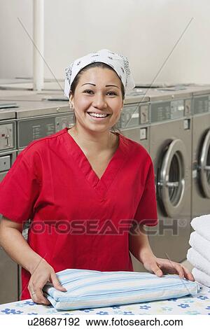 Stock Image - Portrait of a cheerful young woman with towel in Laundromat. Fotosearch