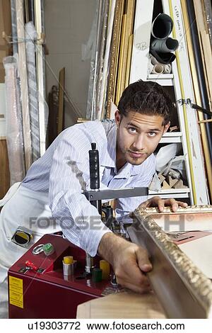 Stock Image - Portrait of a confident craftsman working on picture frame. Fotosearch