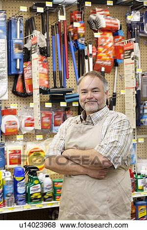 Stock Photo - Portrait of a confident mature salesperson with arms crossed in hardware store. Fotosearch