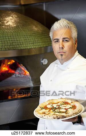 Portrait of a confident mid adult chef holding pizza View Large Photo Image Stock Photo - Portrait of a confident mid adult chef holding pizza. Fotosearch