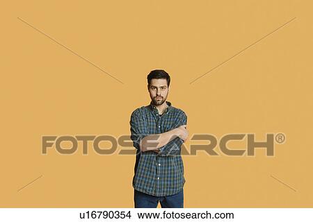 Portrait of a confident young man standing with arms crossed over colored background View Large Photo Image Picture - Portrait of a confident young man standing with arms crossed over colored background. Fotosearch