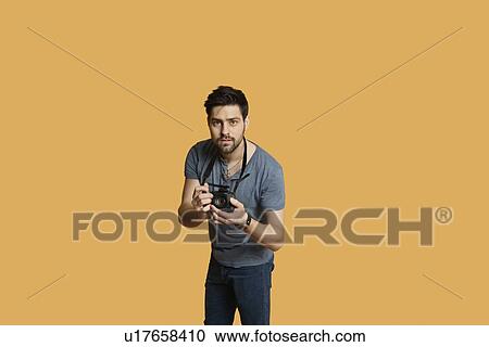 Portrait of a confident young man with camera over colored background View Large Photo Image Stock Image - Portrait of a confident young man with camera over colored background. Fotosearch