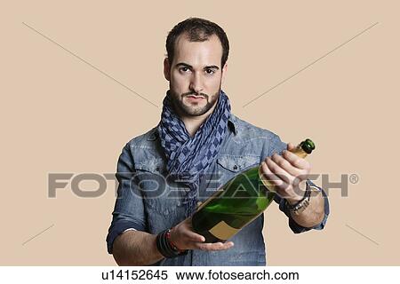 Stock Photography - Portrait of a confident young man with champagne bottle over colored background. Fotosearch