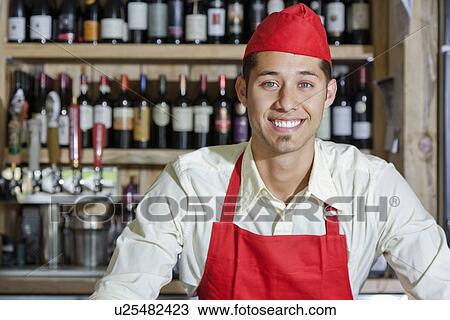 Stock Image - Portrait of a handsome young bartender smiling in bar. Fotosearch