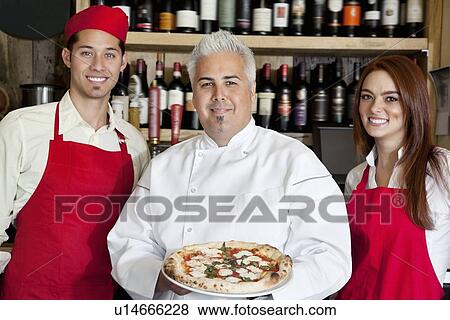 Stock Photo - Portrait of a happy chef holding pizza with wait staff. Fotosearch