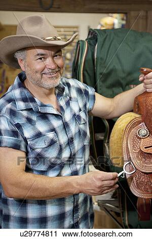 Portrait of a happy cowboy with riding tack in feed store View Large Photo Image Stock Image - Portrait of a happy cowboy with riding tack in feed store. Fotosearch