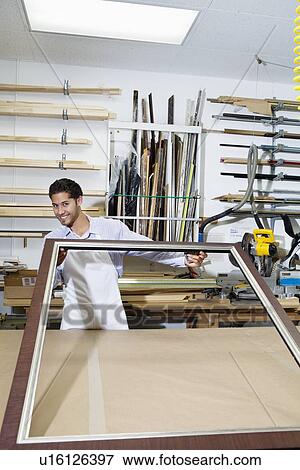 Stock Photo - Portrait of a happy craftsman working on picture frame in workshop. Fotosearch