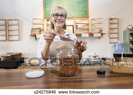 Stock Photograph - Portrait of a happy female employee pouring spice with scoop in jar. Fotosearch