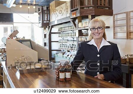 Stock Photo - Portrait of a happy female owner standing at counter with spice jar in store. Fotosearch