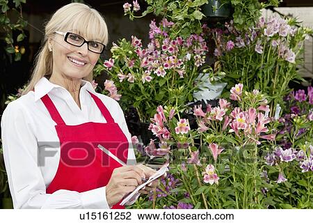 Stock Image - Portrait of a happy florist taking notes in greenhouse. Fotosearch