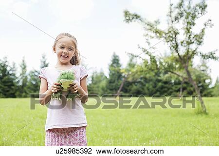 Stock Image - Portrait of a happy girl holding stuffed toy in park. Fotosearch