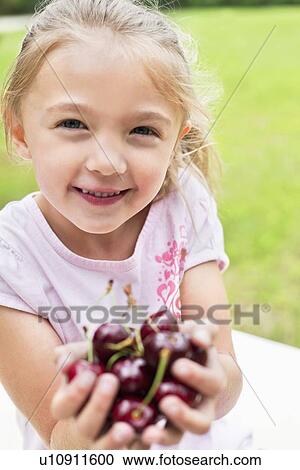 Stock Image - Portrait of a happy girl with hands full on bing cherries. Fotosearch