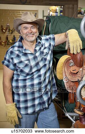 Portrait of a happy mature cowboy standing by saddle in feed store View Large Photo Image Stock Image - Portrait of a happy mature cowboy standing by saddle in feed store. Fotosearch