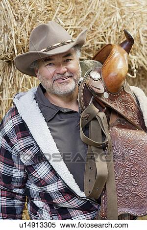Portrait of a happy mature cowboy carrying saddle View Large Photo Image Stock Photography - Portrait of a happy mature cowboy carrying saddle. Fotosearch