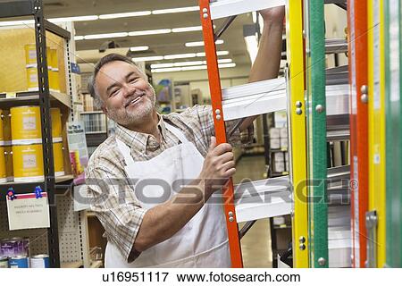 Stock Photo - Portrait of a happy mature man with ladder in hardware store. Fotosearch