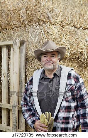 Portrait of a happy mature man with cowboy hat holding gloves in front of hay stack View Large Photo Image Stock Photography - Portrait of a happy mature man with cowboy hat holding gloves in front of hay stack. Fotosearch