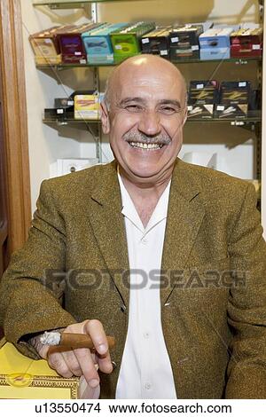 Portrait of a happy mature owner of tobacco shop smoking cigar View Large Photo Image Picture - Portrait of a happy mature owner of tobacco shop smoking cigar. Fotosearch