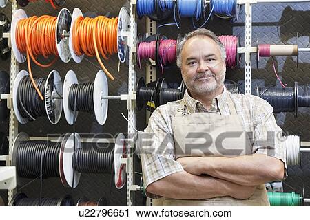 Portrait of a happy mature salesperson standing in front of electrical wire spool with arms crossed in hardware store View Large Photo Image Stock Image - Portrait of a happy mature salesperson standing in front of electrical wire spool with arms crossed in hardware store. Fotosearch