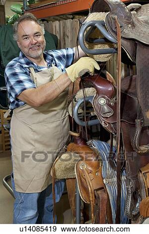 Stock Photo - Portrait of a happy mature salesperson standing by horse riding tack in feed store. Fotosearch