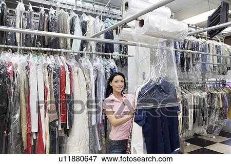 Stock Photo - Portrait of a happy mid adult woman putting plastic to dry cleaned clothes in laundry. Fotosearch
