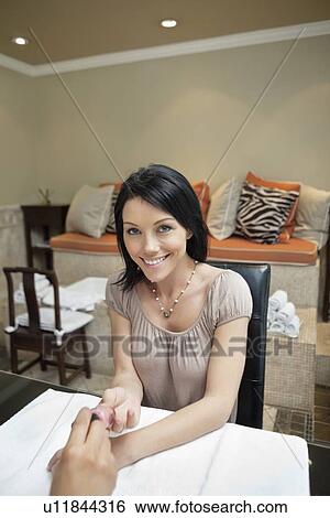 Stock Photograph - Portrait of a happy mid adult woman getting nails polished by manicurist in beauty salon. Fotosearch
