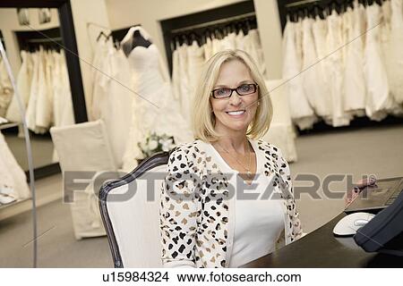 Picture - Portrait of a happy senior woman wearing eyeglasses sitting in bridal store. Fotosearch