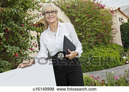 Portrait of a happy senior woman standing by sign board with clipboard View Large Photo Image Stock Photo - Portrait of a happy senior woman standing by sign board with clipboard. Fotosearch