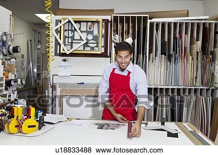 Stock Photo - Portrait of a happy skilled worker measuring with meter stick in workshop. Fotosearch