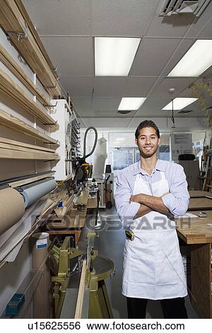 Stock Photograph - Portrait of a happy skilled worker standing with arms crossed in workshop. Fotosearch