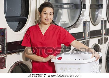Stock Photo - Portrait of a happy woman carrying laundry basket with washing machine in background. Fotosearch