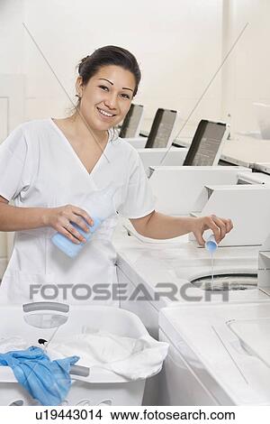 Portrait of a happy woman employee pouring detergent in washer View Large Photo Image Picture - Portrait of a happy woman employee pouring detergent in washer. Fotosearch
