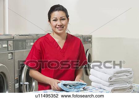 Stock Image - Portrait of a happy woman in red uniform with towel in Laundromat. Fotosearch