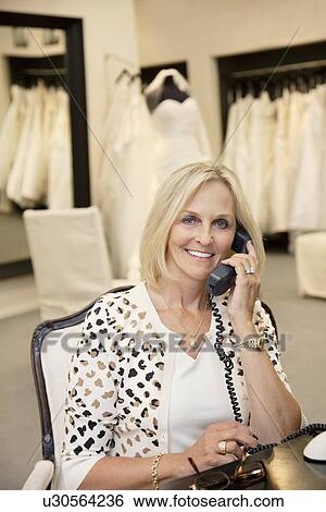 Stock Photograph - Portrait of a happy woman listening to telephone receiver in bridal store. Fotosearch