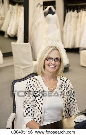 Stock Photograph - Portrait of a happy woman sitting on chair in bridal store. Fotosearch