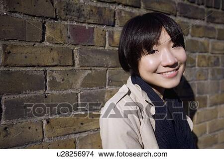 Portrait of a happy young Asian woman against wall View Large Photo Image Picture - Portrait of a happy young Asian woman against wall. Fotosearch