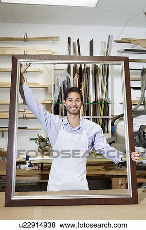 Portrait of a happy young craftsman holding big frame in workshop View Large Photo Image Stock Photo - Portrait of a happy young craftsman holding big frame in workshop. Fotosearch