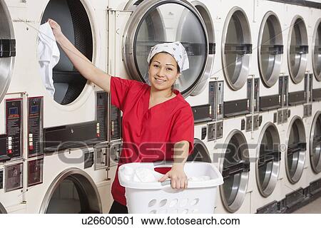 Stock Image - Portrait of a happy young female employee putting clothes in washer. Fotosearch