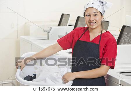 Portrait of a happy young female employee carrying laundry basket with washing machines in background View Large Photo Image Stock Photography - Portrait of a happy young female employee carrying laundry basket with washing machines in background. Fotosearch